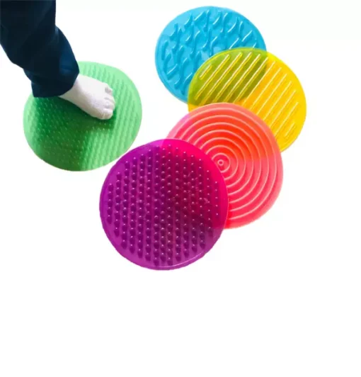 Recurso terapêutico Tapete Sensorial, um conjunto com 5 tapetes sensoriais com texturas diversas, em forma circular e nas cores verde, roxo, amarelo, azul e vermelho.